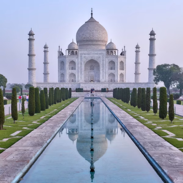 The Taj Mahal in Agra, India, reflected in the central water canal with symmetrical Mughal gardens and historic white marble architecture.