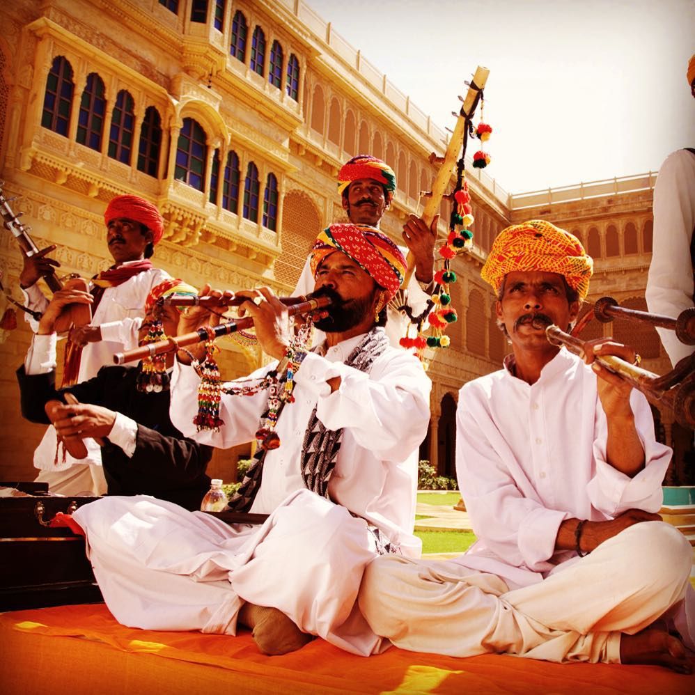 Traditional Rajasthani folk musicians performing with cultural instruments in front of a heritage palace in Rajasthan, India.
