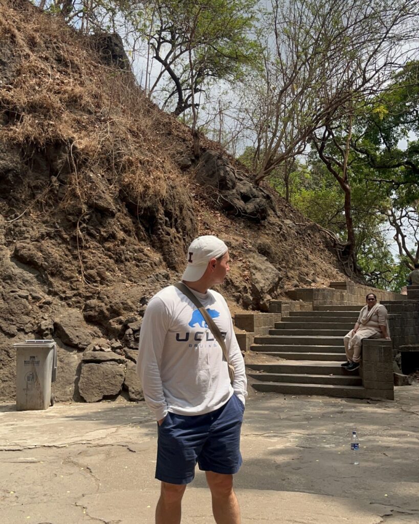 Tourist exploring rocky hillside path in Mumbai with a local guide in the background.